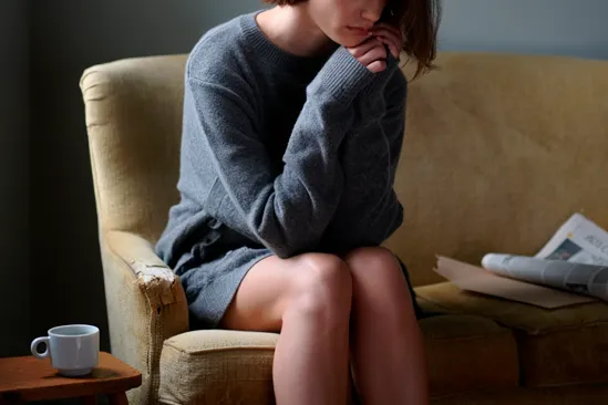 Женщина сидит на диване с грустным лицом Женщина грустит